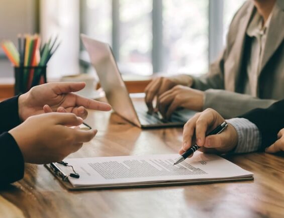 Business professionals reviewing and signing commercial loan documents during a financing meeting.